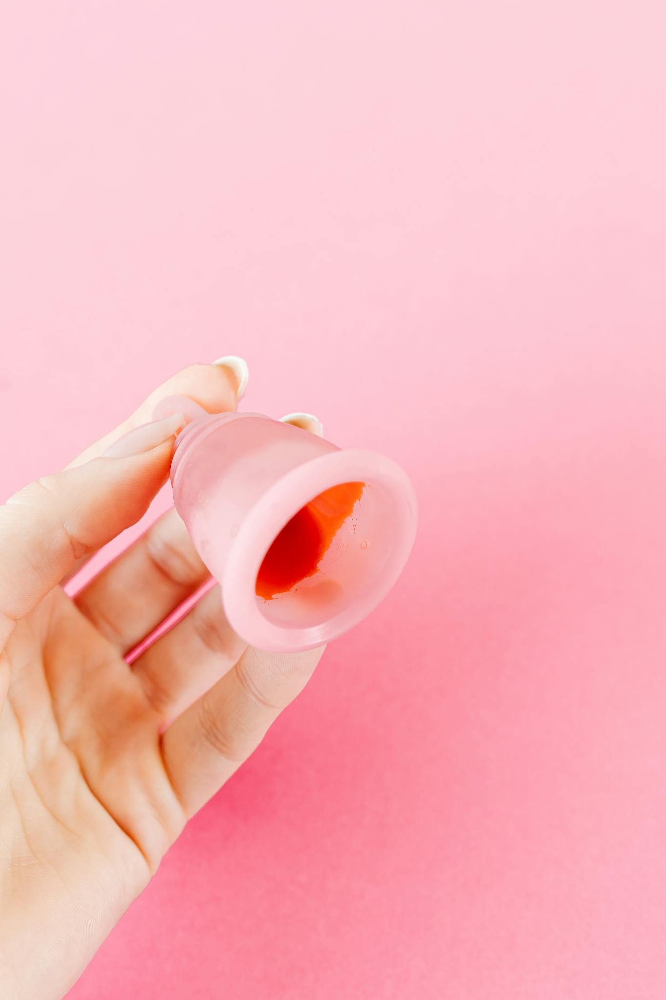 A close-up of a hand holding a pink menstrual cup against a matching background.