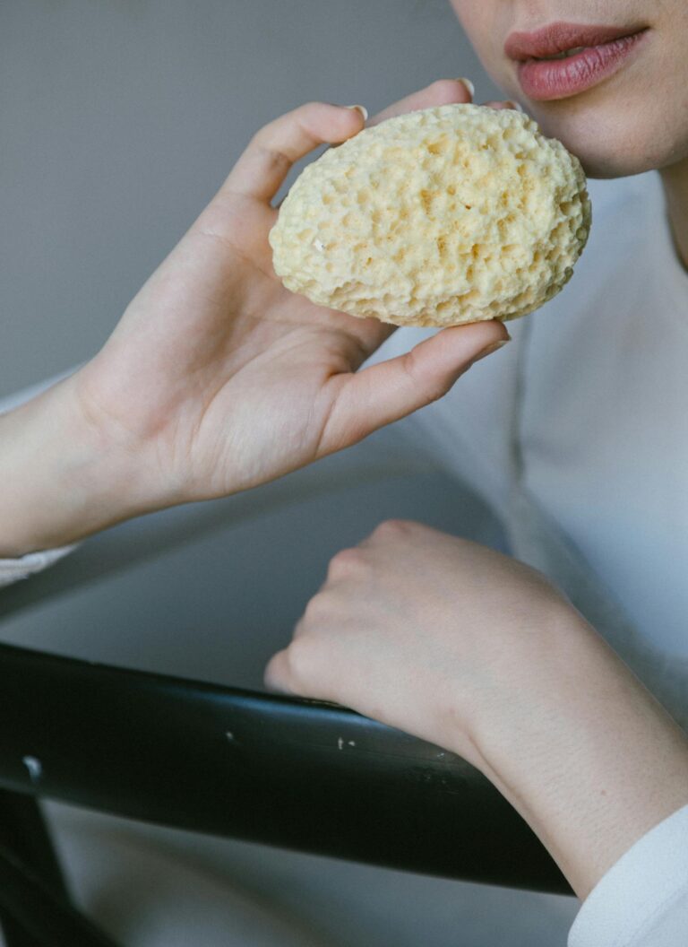 A natural sponge held by a woman's hand in a serene setting.