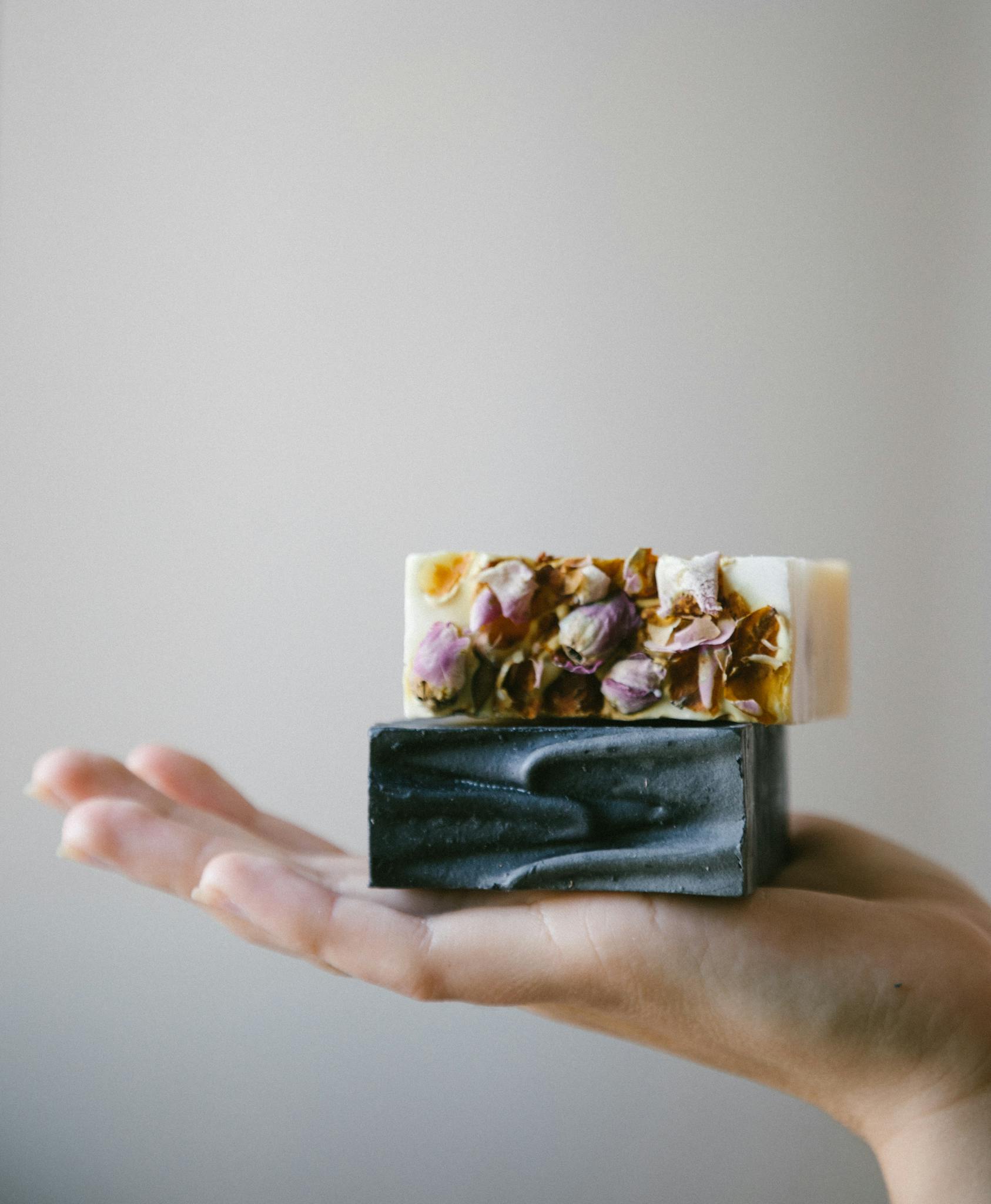 Hand holding handcrafted floral and charcoal soaps, embodying natural skincare and sustainable beauty.