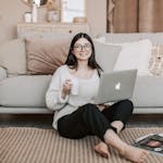 Happy woman enjoying coffee while using a laptop in a cozy living room setting.