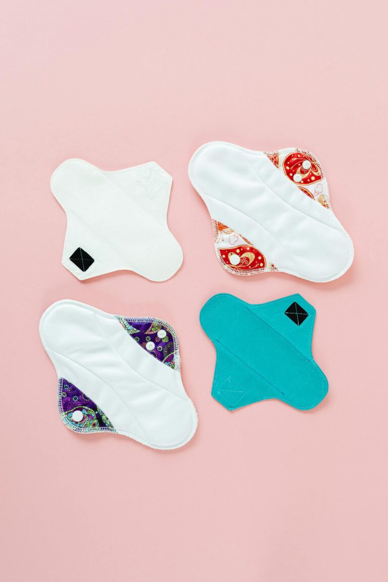 Top view of four colorful reusable menstrual pads on a pastel pink background, eco-friendly and sustainable health products.